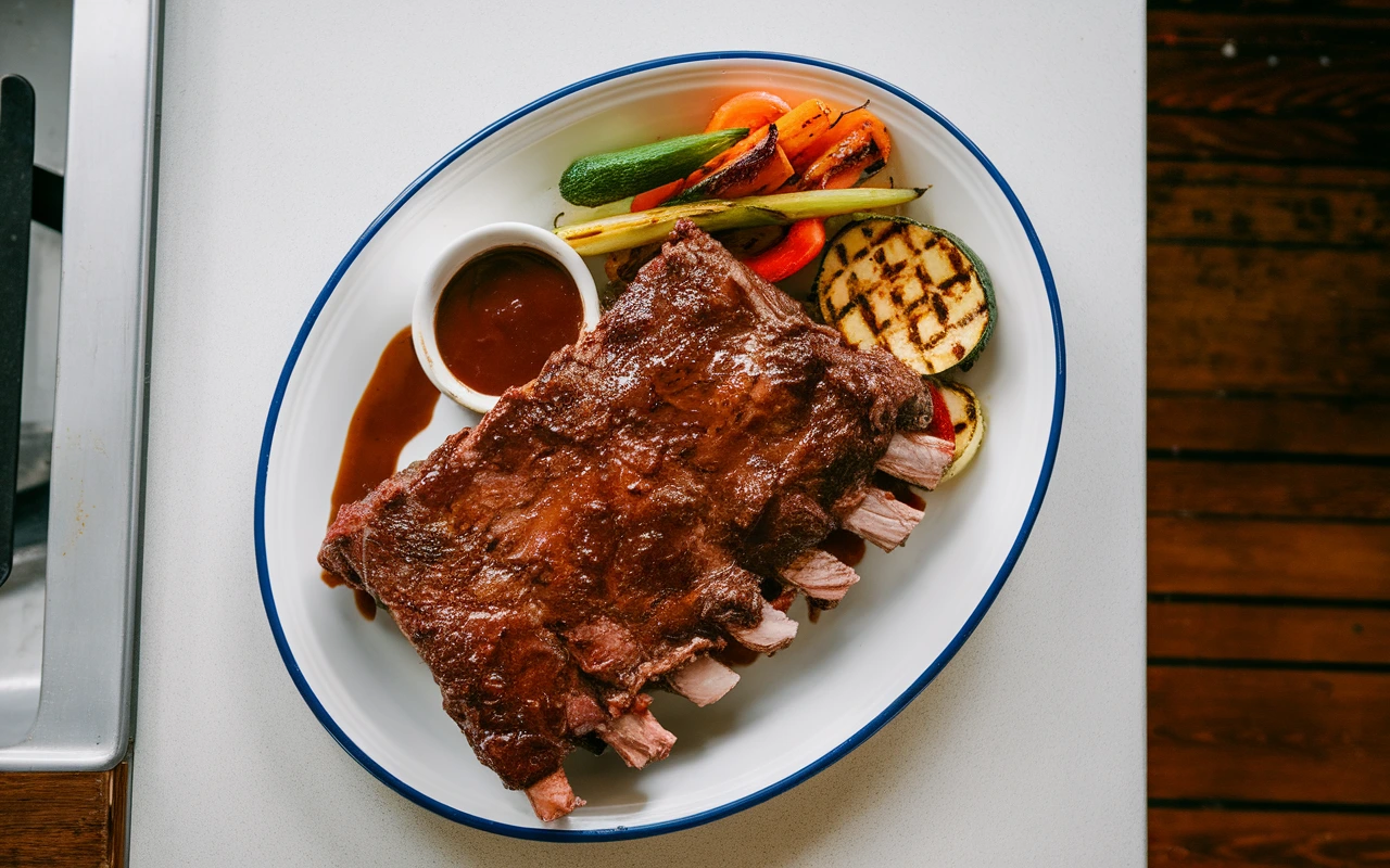 Juicy beef back ribs served with grilled vegetables and barbecue sauce on a white plate