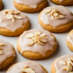 Soft almond sugar cookies with a light glaze and sliced almonds on top, arranged on a baking sheet